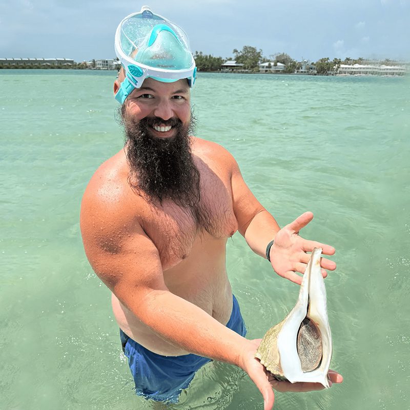 Smiling man displaying seashell in ocean