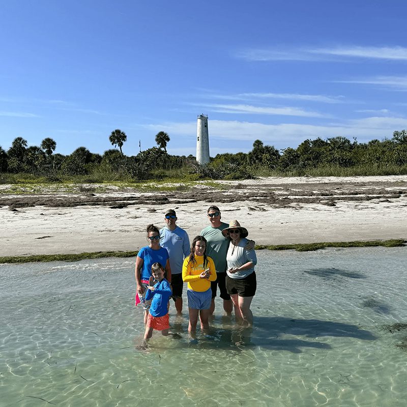 People posing on sunny beach with lighthouse