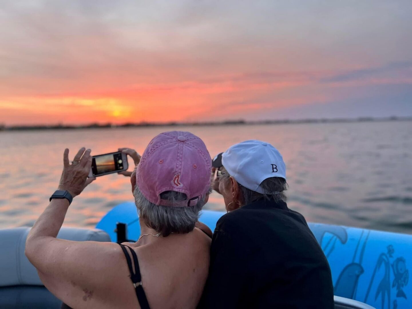 Two women photographing sunset from boat
